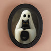 An oval decorative ornament featuring a ghost figure with white drapery and a black cat looking out.