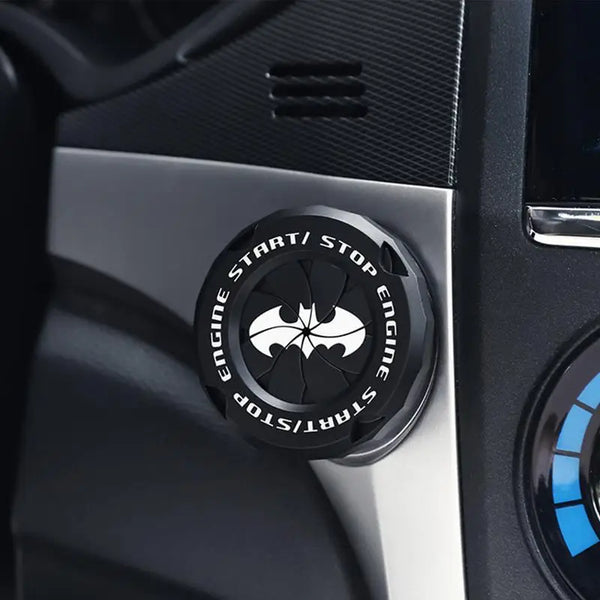 Close-up of a black push start/stop button cover with a bat emblem on a car interior panel.
