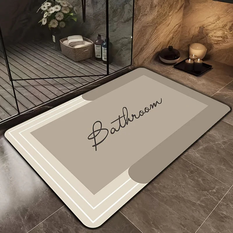 A rectangular beige bath mat with a delicate script reading Bathroom is placed on a tiled floor near a glass shelf.