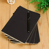 A stack of black A6 kraft paper blank notebooks with a black pen resting on top on a wooden surface.