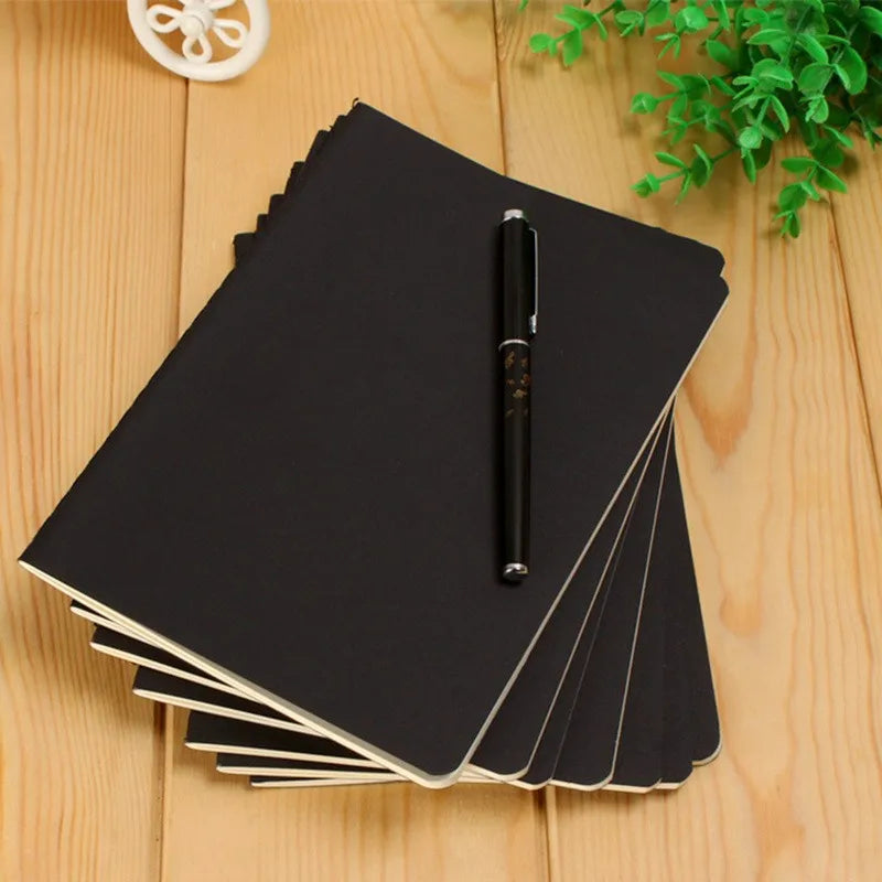 A stack of black A6 kraft paper blank notebooks with a black pen resting on top on a wooden surface.