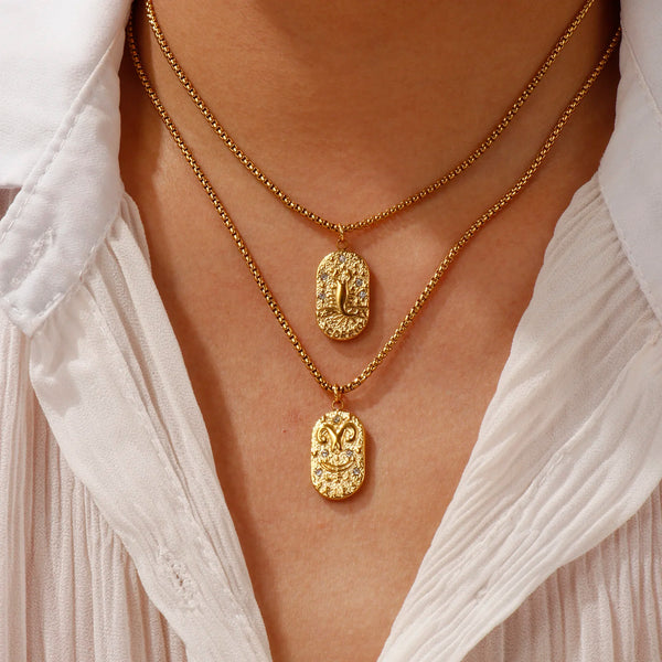 A close-up of a gold plated constellation pendant necklace worn around the neck against a white shirt.