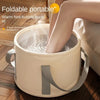 A person is soaking their feet in a portable, foldable insulated foot soak tub made of light beige material.