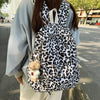 A person wearing a light blue jacket is carrying a leopard print nylon backpack with multiple pockets.