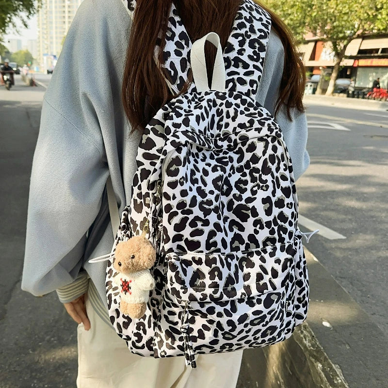 A person wearing a light blue jacket is carrying a leopard print nylon backpack with multiple pockets.
