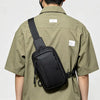 Eine Person trägt eine schwarze, vielseitige Unisex-Crossbody-Tasche über der Brust auf dem Rücken, wobei sie ein olivgrünes 