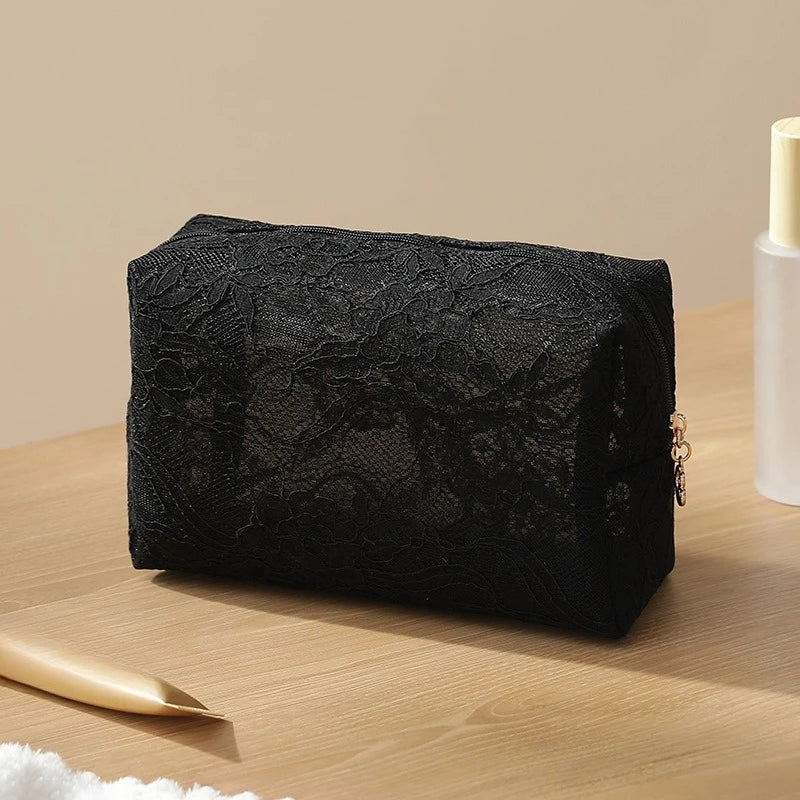 Black lace mesh makeup bag resting on a wooden surface with a gold applicator nearby.