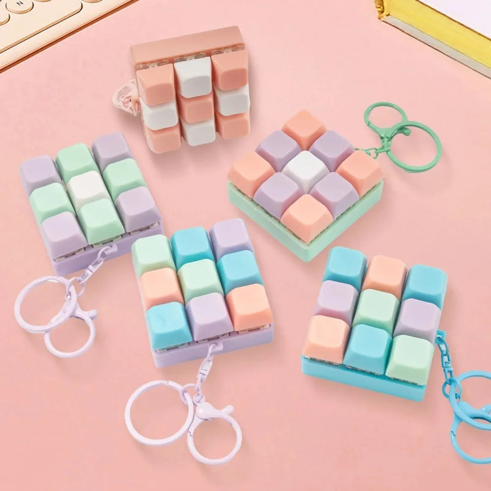 A collection of pastel colored mini keyboard fidget keychains arranged on a pink background.