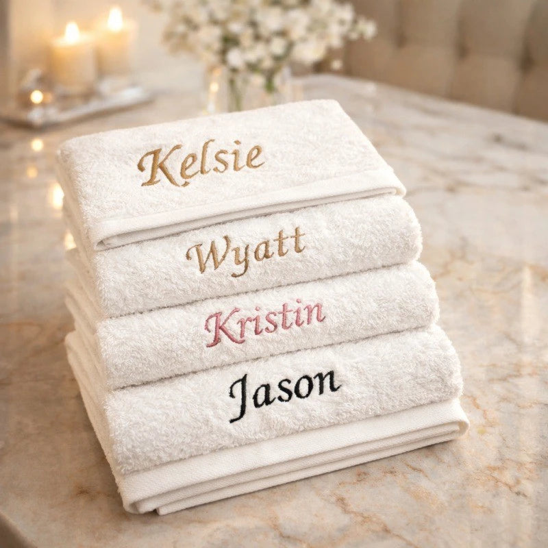 A stack of four white organic cotton face towels with names printed on them resting on a marble surface.