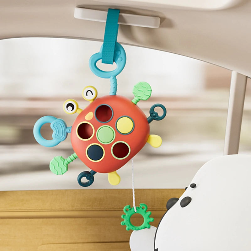 A silicone pull string sensory toy with multiple colored holes hangs from a white car interior panel.