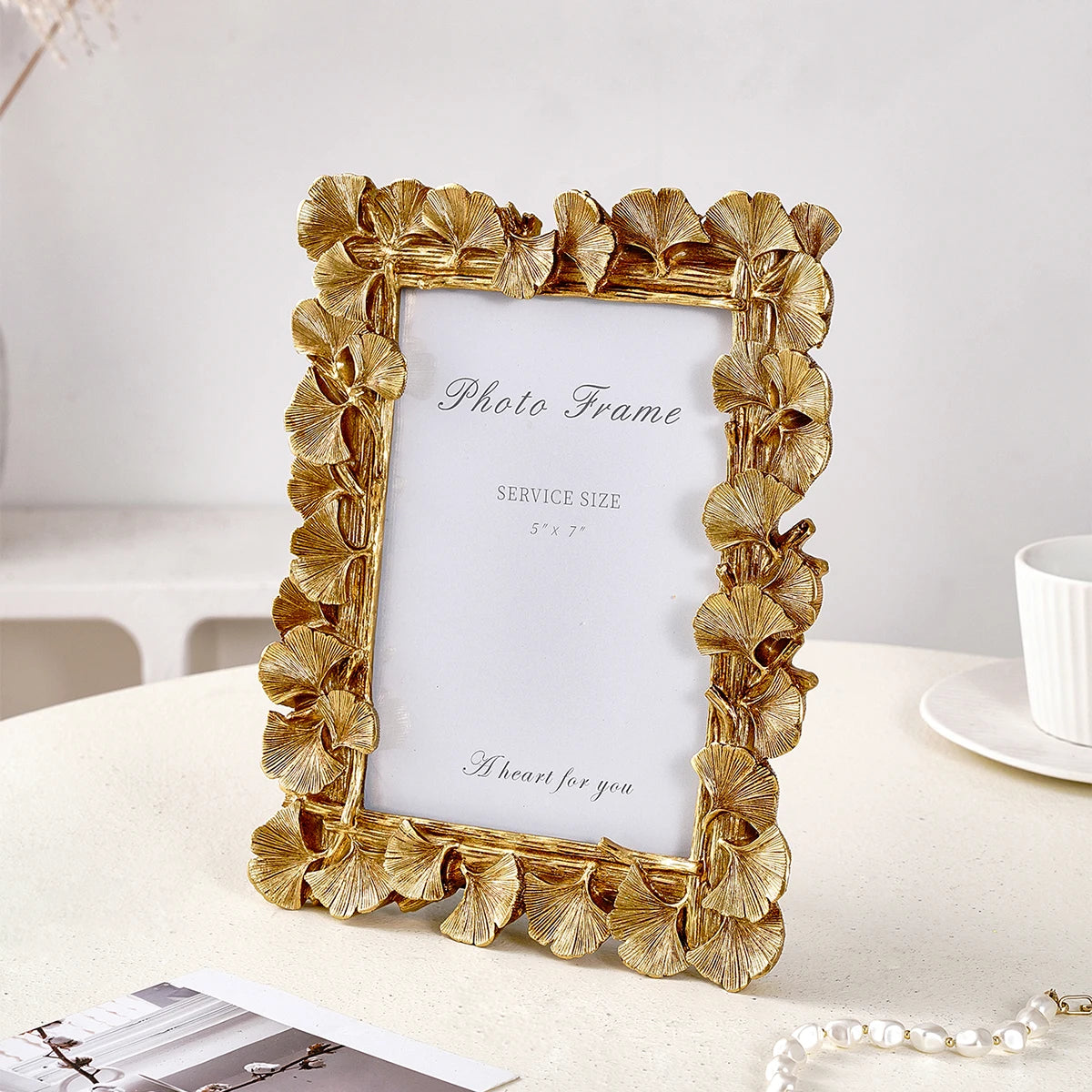An elegant golden ginkgo leaf resin photo frame displayed on a white table.