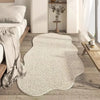 A light beige irregular area rug with a plush texture placed on a wooden floor next to a bed and white walls.