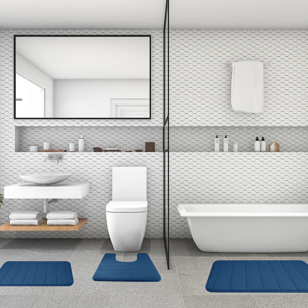 A modern bathroom featuring a white toilet, vanity, and bathtub with blue non-slip bath mats on the floor.