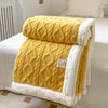 A yellow double-layer fleece throw blanket with white sherpa trim resting on a white bed.