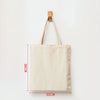 A beige reusable canvas shopping tote bag hanging on a wooden hanger.