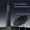 A black umbrella with a widened strap and automated mechanized handle is shown open against a dark background.