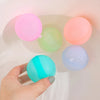 Eine Hand hält einen leuchtend blauen Silikon-Wasserball neben rosa, grüne und orangefarbene Ballons in einer weißen Schale.