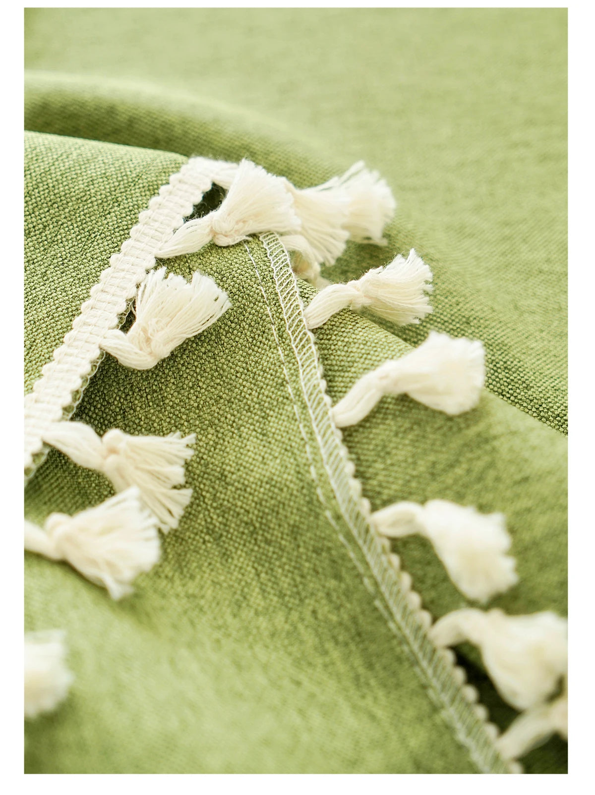 Close-up of a sage green farmhouse tablecloth featuring white cotton tassels along the edge.