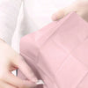 A hand is holding a pink disposable toilet seat cover, showing its texture and folded shape.