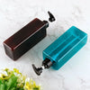 Three refillable soap dispenser bottles in dark brown and teal glass on a white marble surface.