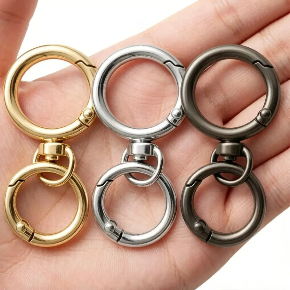 Three round spring snap hooks in gold and silver metal alloy carabiners shown on a hand.