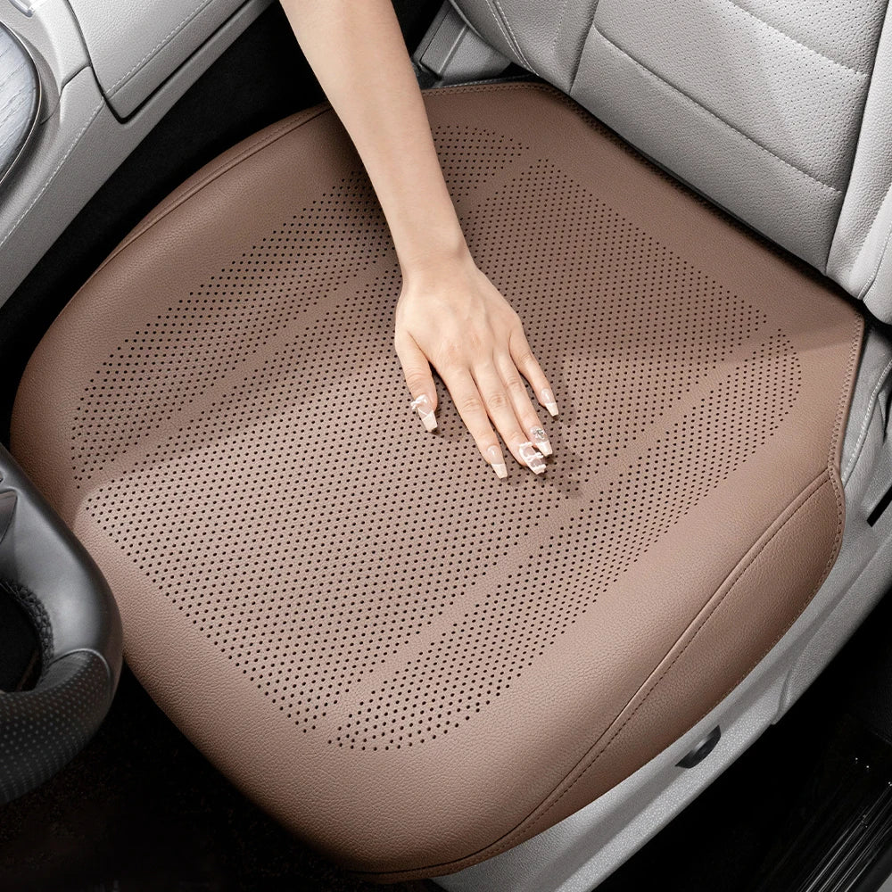 A hand rests on a tan breathable leather car seat cushion inside a vehicle interior.