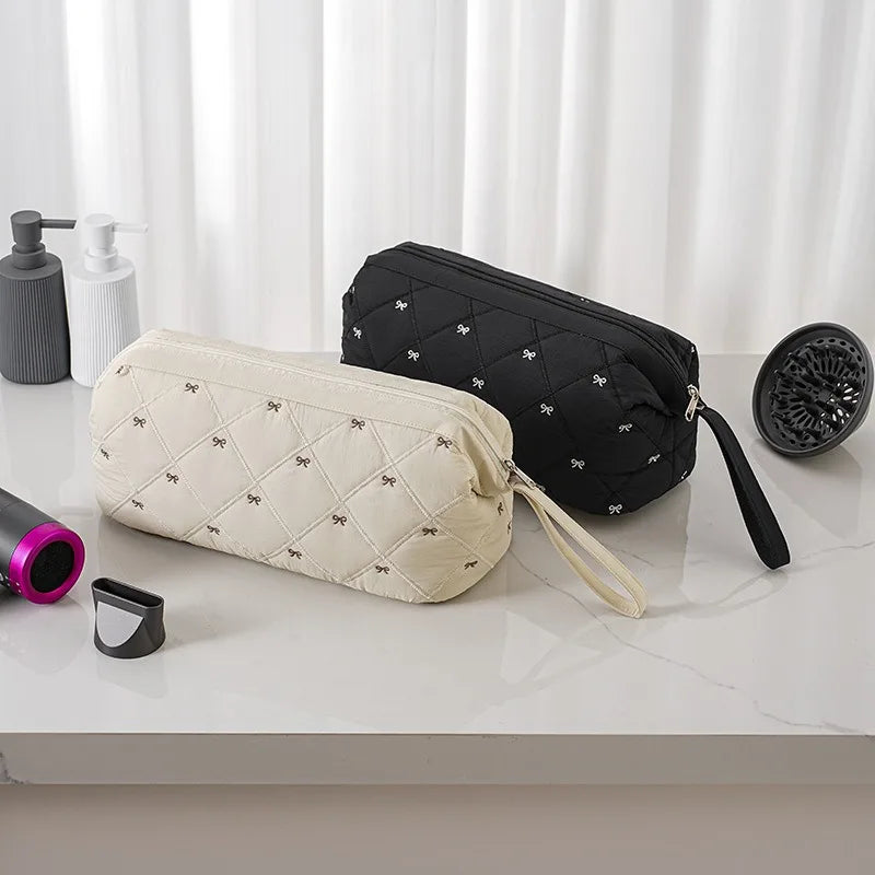 Two fabric storage bags, one beige quilted and one black, are displayed on a white surface.