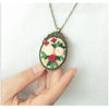 A close-up of a silver necklace featuring floral embroidery patterns on a green background.