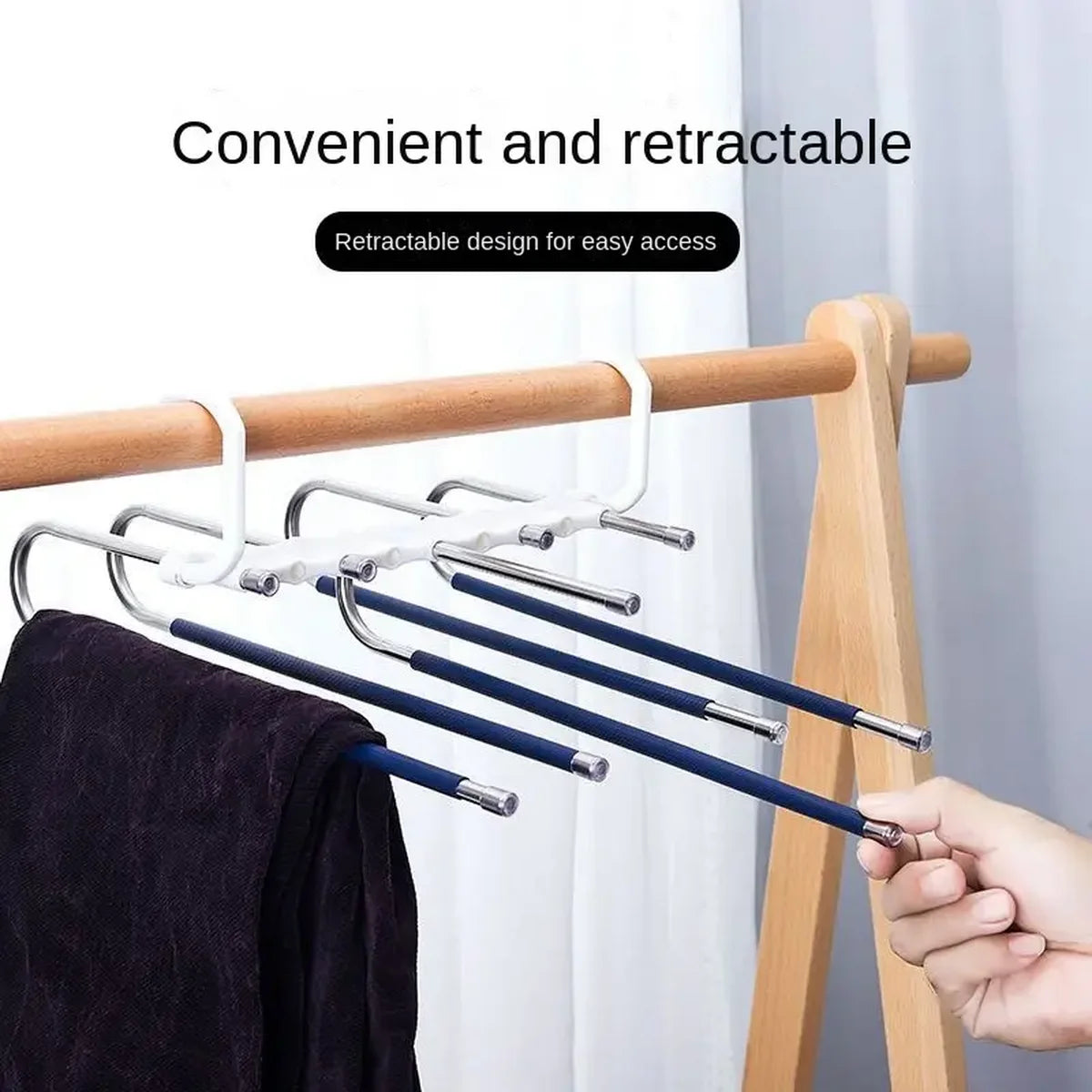 A close-up of a retractable stainless steel pants hanger with multiple layers being used on a wooden rack.