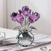 A crystal rose sculpture with a bouquet of purple and pink reflective flowers displayed in a clear glass vase.