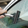 A hand uses a black retractable car mirror and window cleaning wiper to wipe water off a car window.