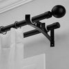A black curtain rod bracket with a spherical finial is mounted on a white wall.