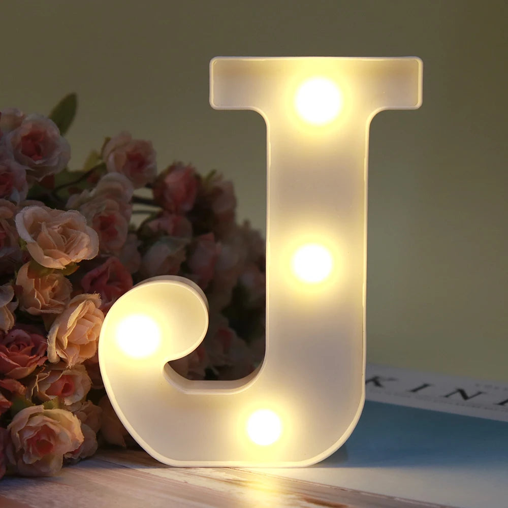 Lumière de nuit alphabet LED blanche en forme de lettre J, éclairant une surface en bois.