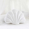 A white velvet decorative shell print throw pillow resting on a white surface.