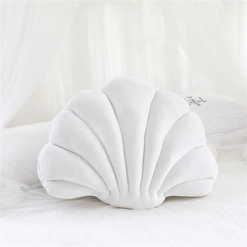 A white velvet decorative shell print throw pillow resting on a white surface.
