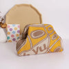 A yellow and beige hand-knit clutch bag with pearl accents resting in front of a light beige card.