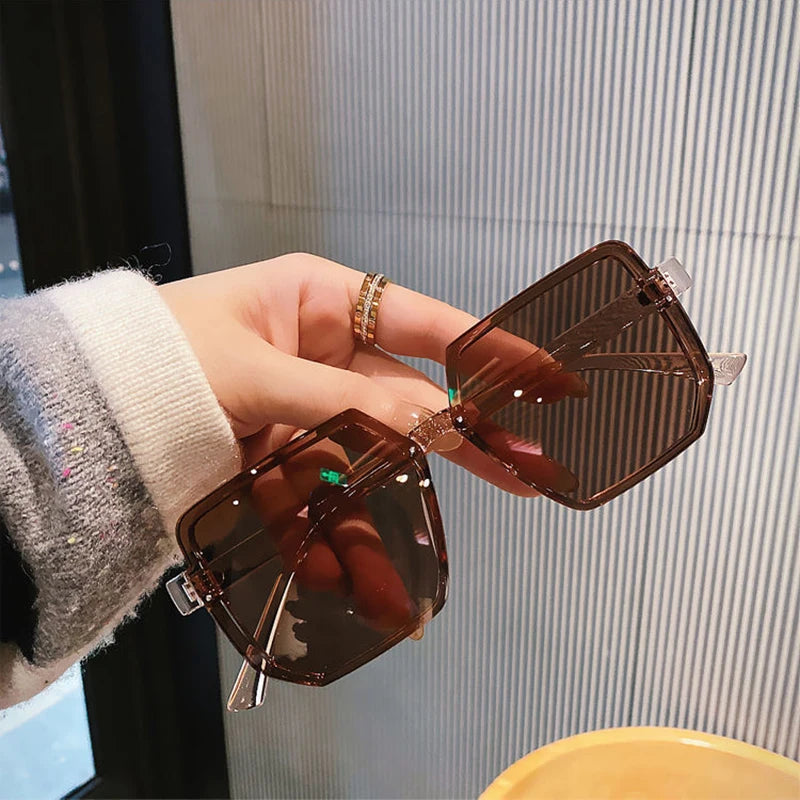 Una mano sostiene unas gafas de sol cuadradas marrones vintage contra un fondo a rayas.
