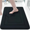 A black absorbent soft non-slip bath mat is placed on a white tiled floor, with a person's foot resting on it.