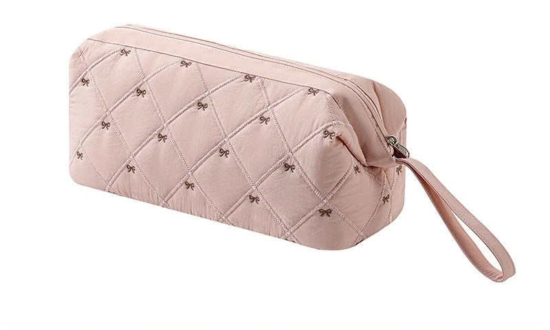 A light pink quilted storage bag for a portable hair dryer and styling tool with a fabric strap.