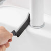 A hand is using a black grout cleaning brush with hard bristles on a white ceramic fixture.