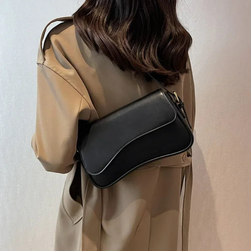 A woman is holding a black vintage leather crossbody bag with a flap closure under a beige trench coat.