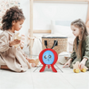 Two young girls play with a red balloon burst game on the floor in a bright room.