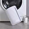 A white mesh shoe washing bag with a zipper closure is shown next to a white appliance.