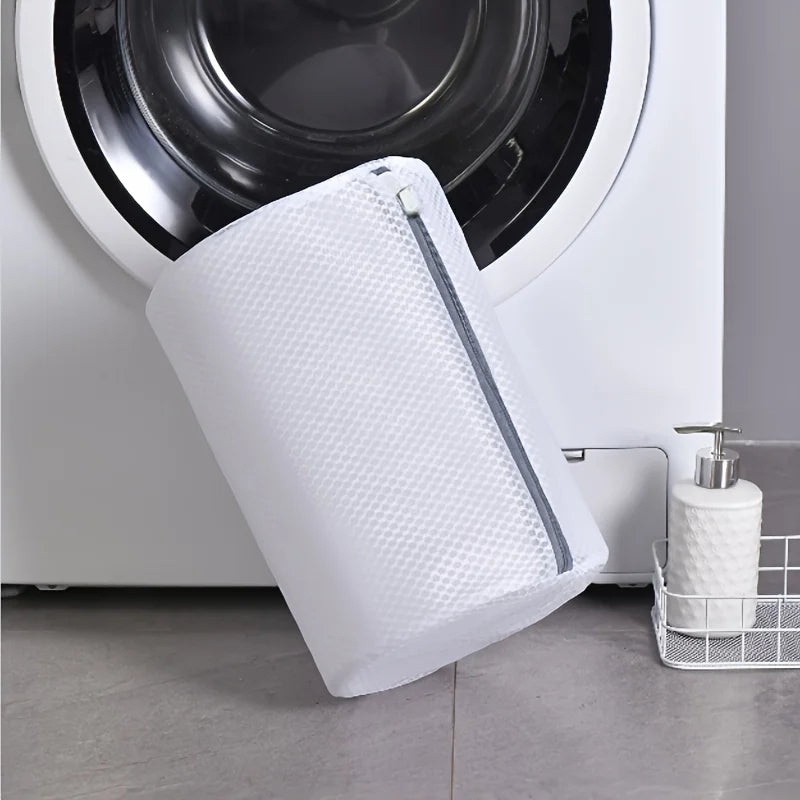 A white mesh shoe washing bag with a zipper closure is shown next to a white appliance.