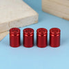A set of four shiny red bullet shell tire valve stem caps resting on a light blue surface next to a wooden block.