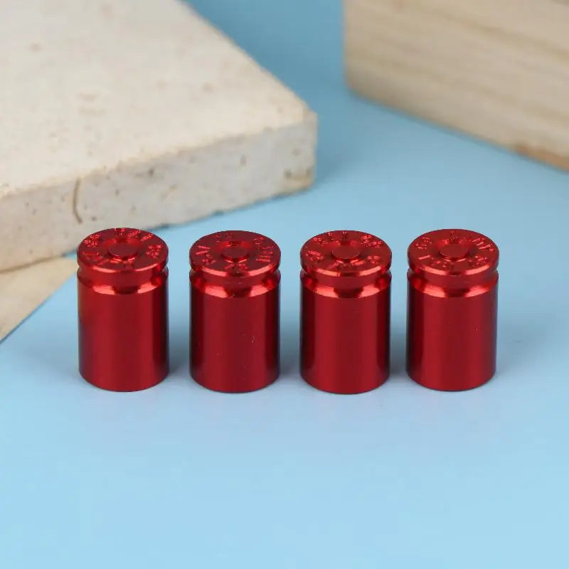 A set of four shiny red bullet shell tire valve stem caps resting on a light blue surface next to a wooden block.