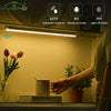 A close-up of a white LED light fixture mounted above a shelf, illuminating a room with plants and a mug.