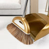 A gold-colored broom and dustpan set with a floor wiper resting on a white floor.