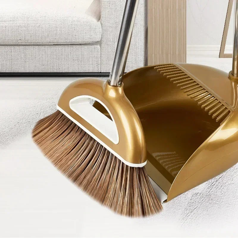 A gold-colored broom and dustpan set with a floor wiper resting on a white floor.