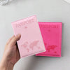 A hand holds a pink passport holder with a world map design on the cover.
